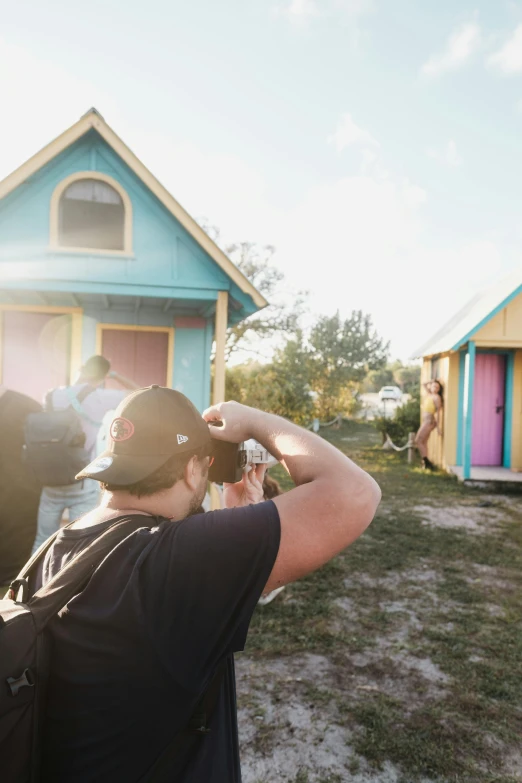 man in baseball cap standing in front of two brightly colored tiny houses