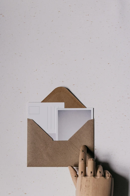 a small wooden hand holding an envelope with a sheet of paper in front of it
