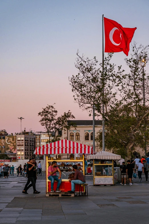 people walking and sitting in a kiosk stand with a red flag