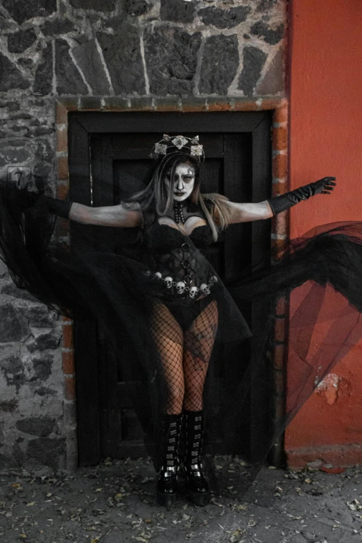 a woman dressed up as a demon standing in front of an entrance with her arms out and her body wrapped up and wearing a black dress