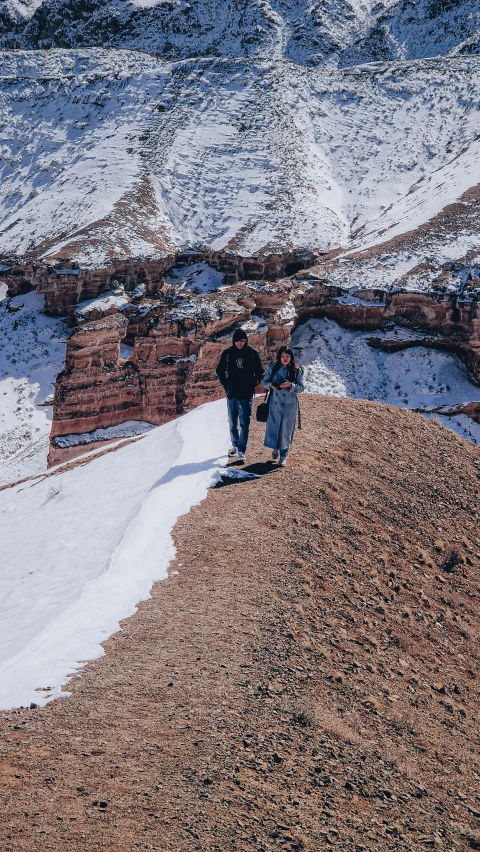two people walking down the side of a snow covered mountain