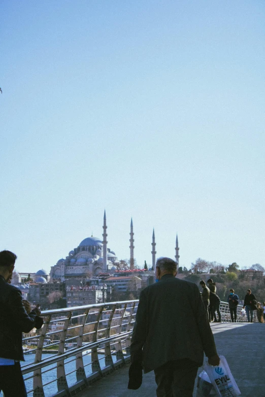 a group of people walking across a bridge with buildings in the background