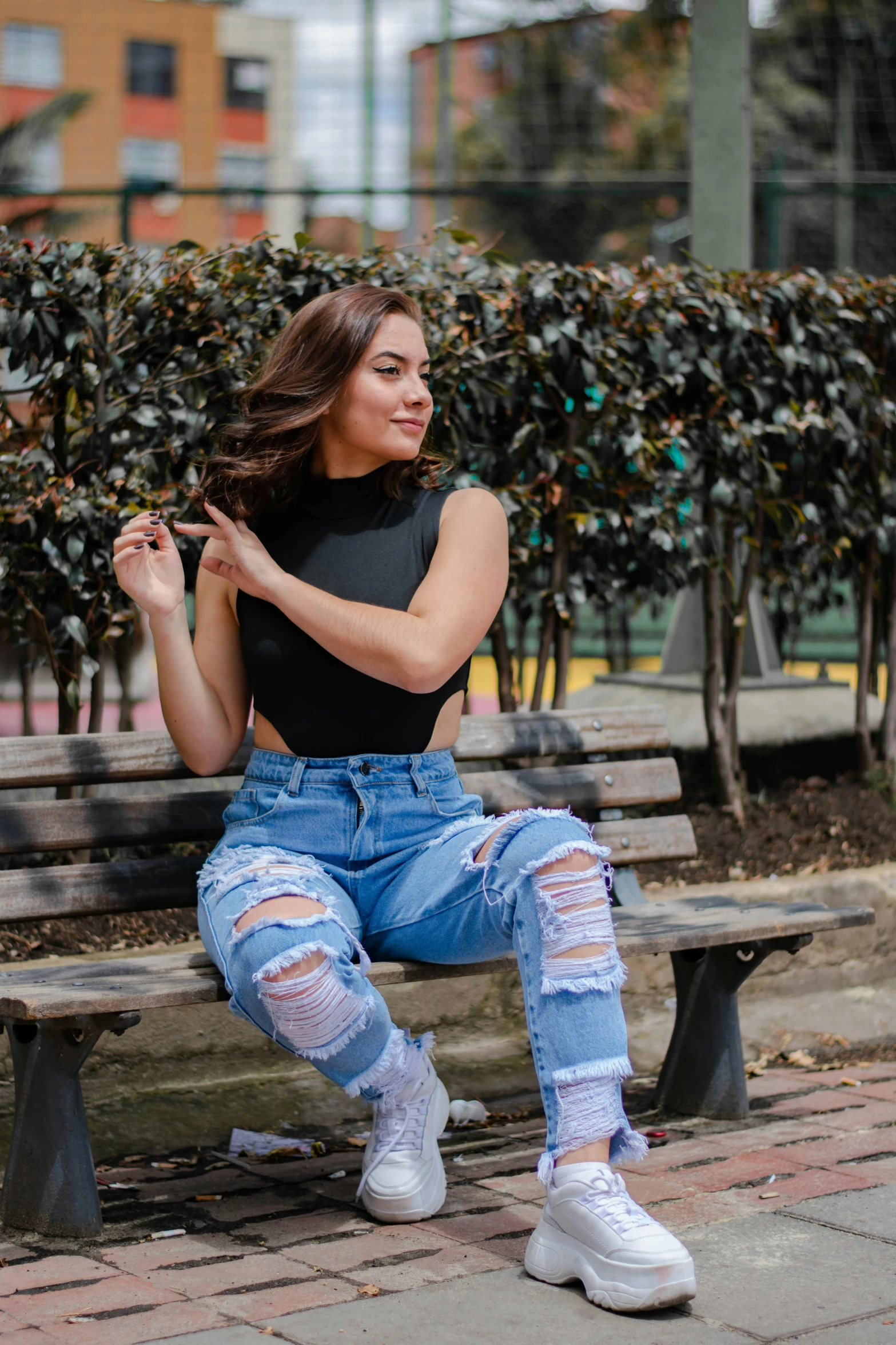 a young woman with ripped jeans, black tank top and sneakers sitting on a bench