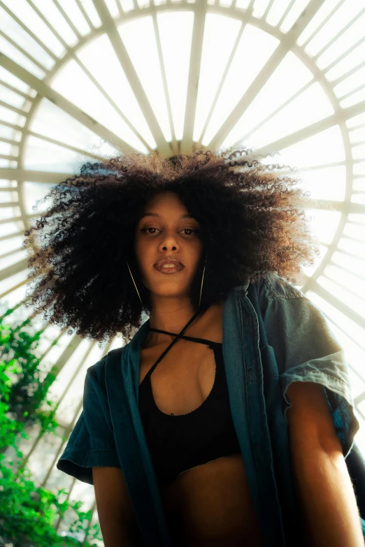 woman with large afro and green jacket posing near large building