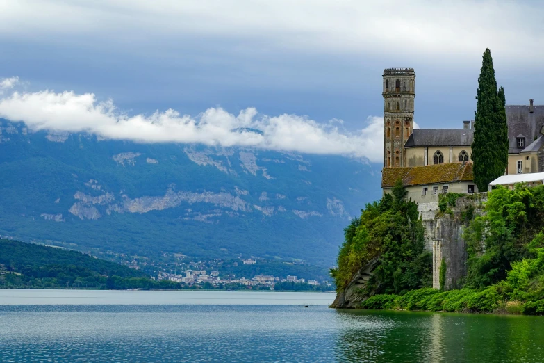 a castle is seen on the bank of the water with mountains in the background