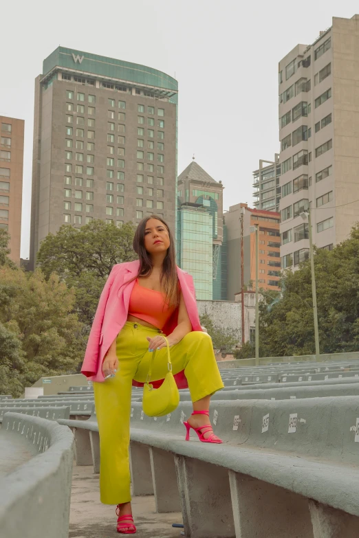 a woman is posing in the city in her pink blazer and yellow pants