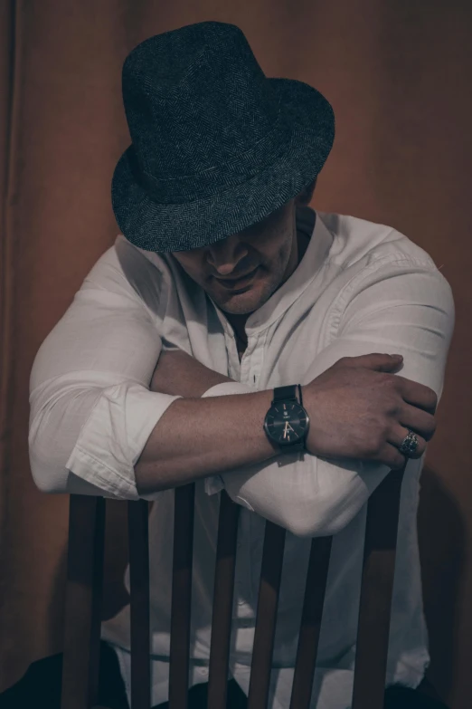 a man in white shirt sitting in chair wearing hat and watch