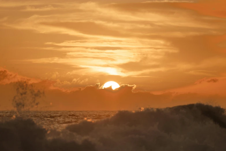 the sun rises behind a large cloud over some water