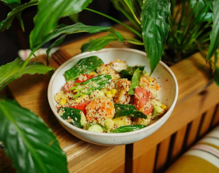 a white bowl with some cooked vegetables and a green plant