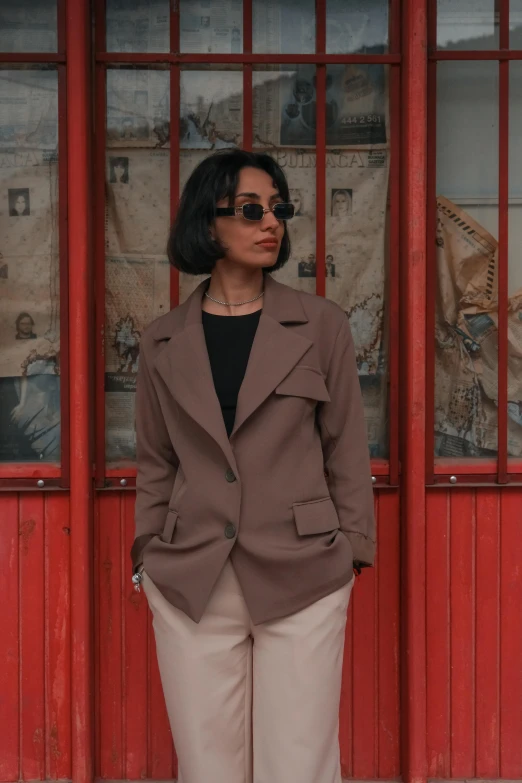 a young woman wearing sunglasses, standing next to a wall