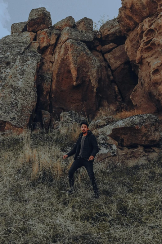 a man is standing in the grass by large rocks