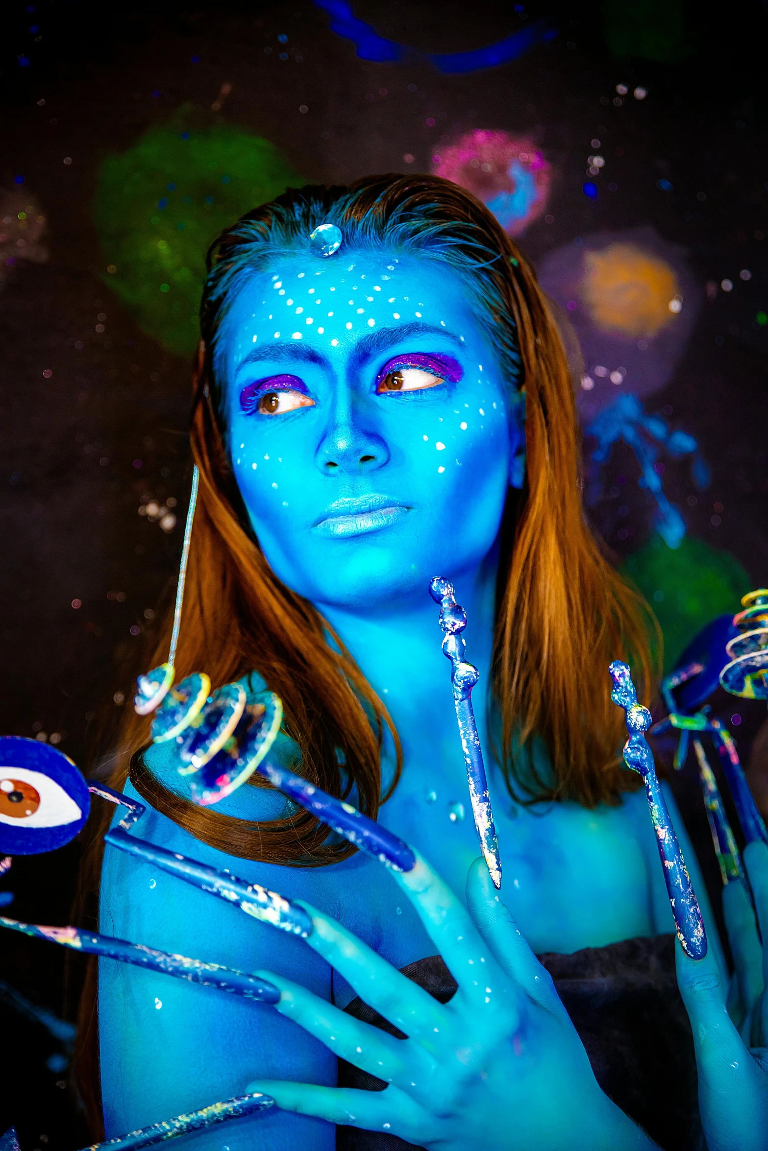 a woman with blue makeup holding spoons next to a blue - lit background