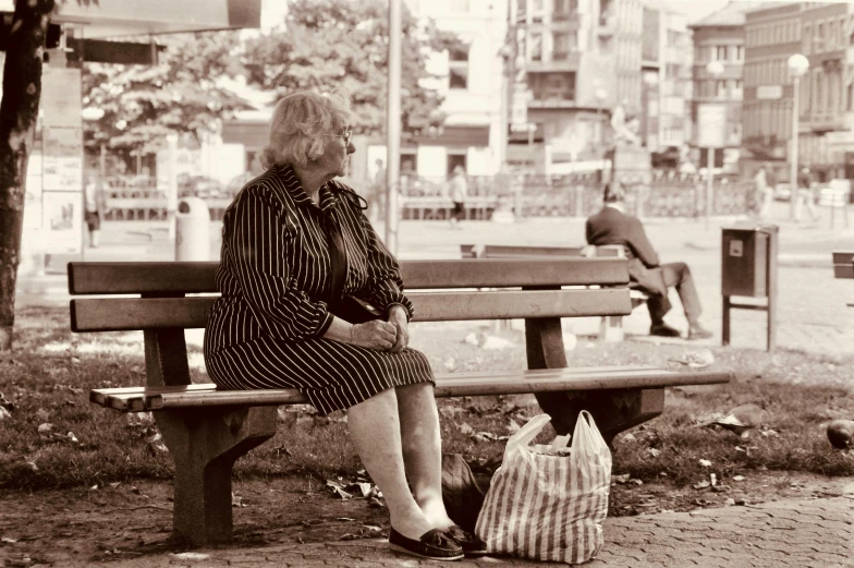 an older woman sits on a park bench with her bag