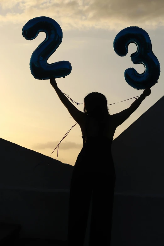 a silhouette picture of a woman holding two balloons