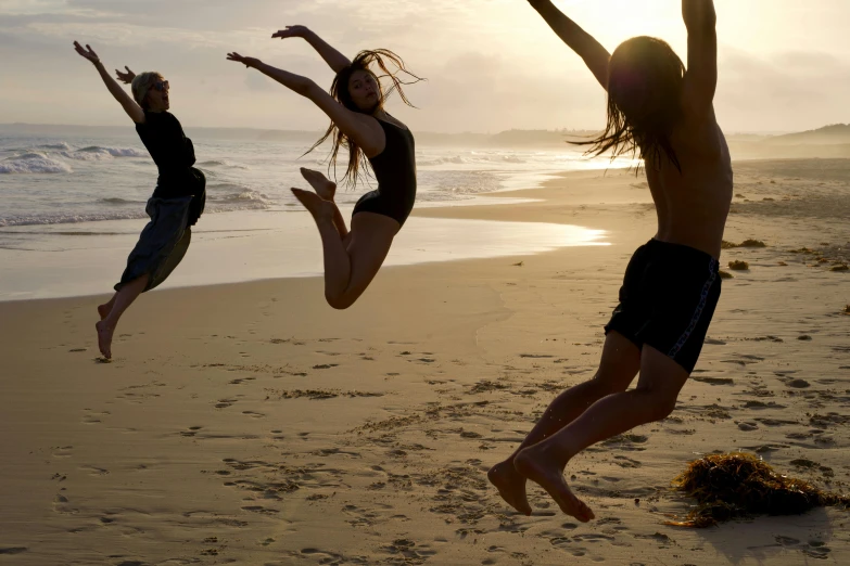 two people jump on the beach in front of the ocean