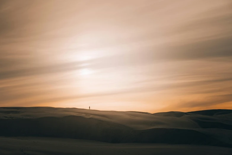 a single person walking down a sandy hillside under a cloudy sky