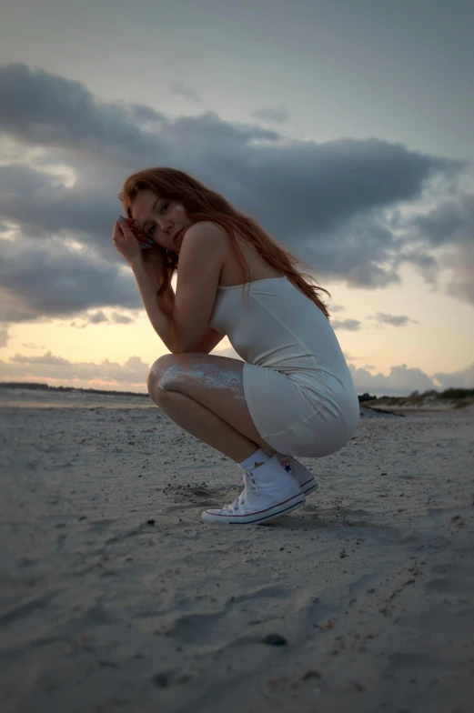 a beautiful young woman sitting on the sand on a beach