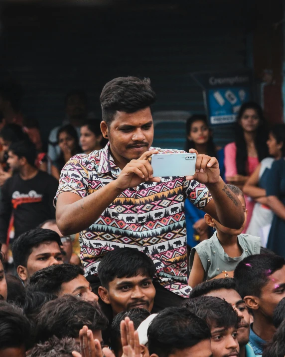 a man in a colorful shirt holds up a cellphone