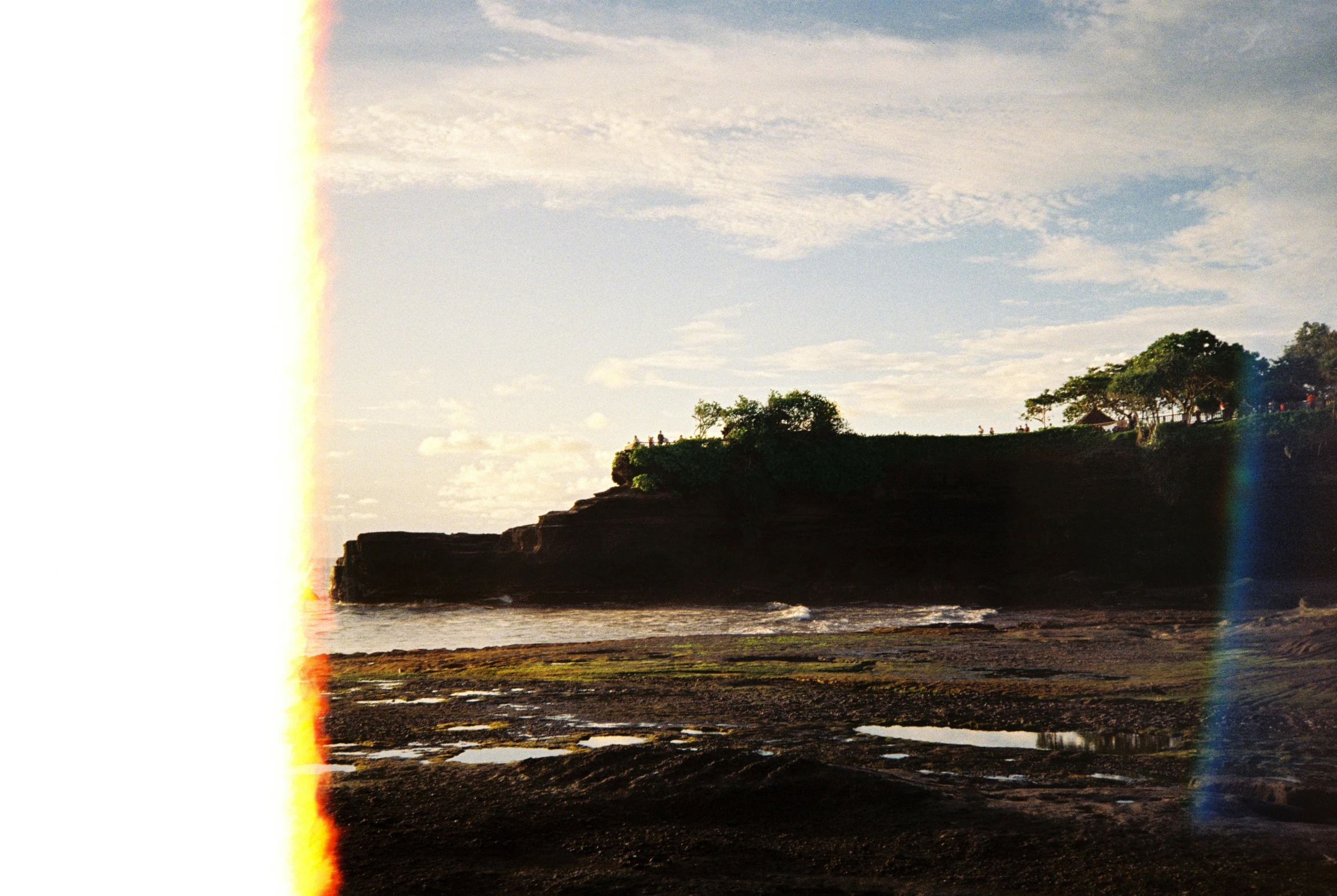 a rainbow shines in front of a green hill next to the ocean