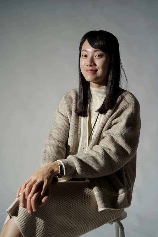 a woman sitting on a stool in her beige outfit