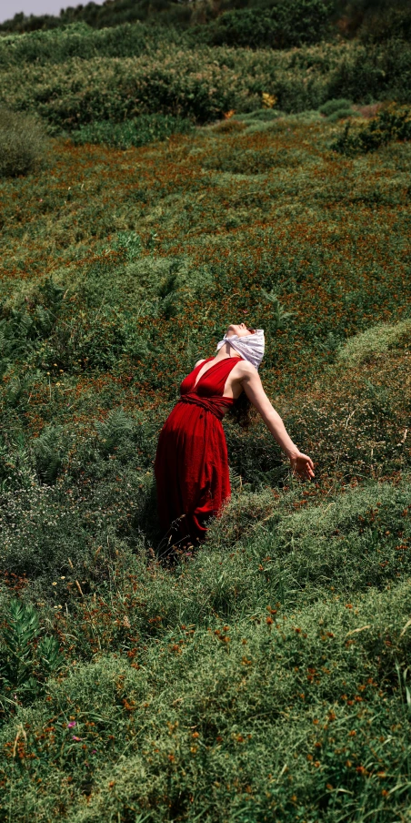 woman in red dress crouching down to pick up soing on a hill