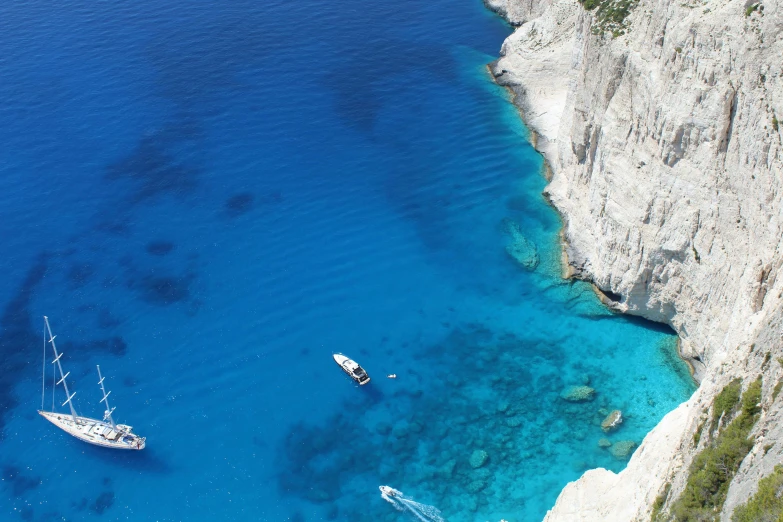 several boats floating in a lake near a rocky cliff