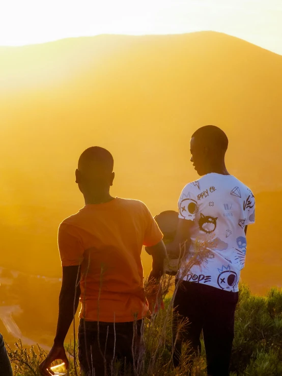 two people are standing near a hill with the sun setting in the background