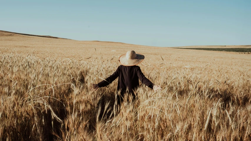 a woman wearing a hat walking across a large field of grass
