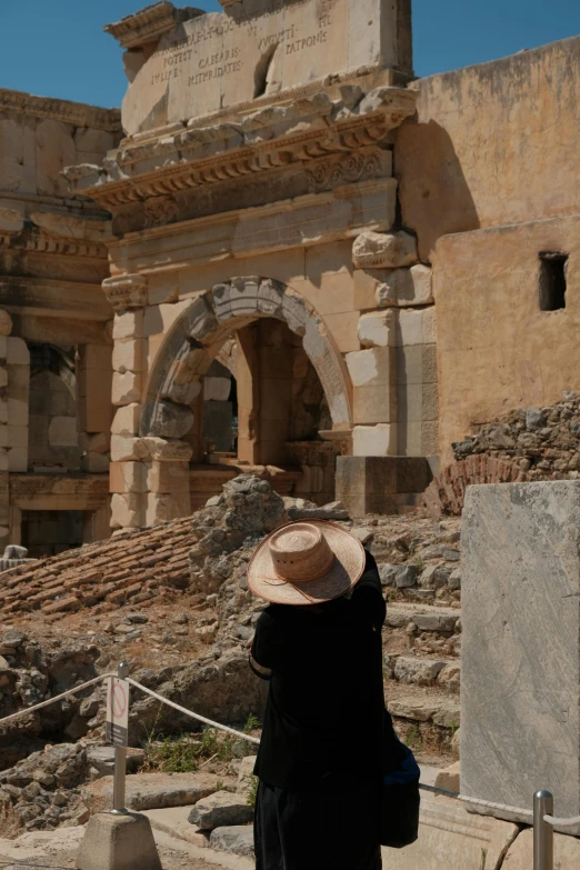 a man wearing a straw hat is taking a picture of ruins