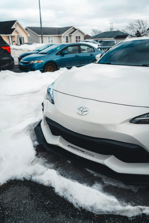 the front of a white sports car parked on a snow covered parking lot