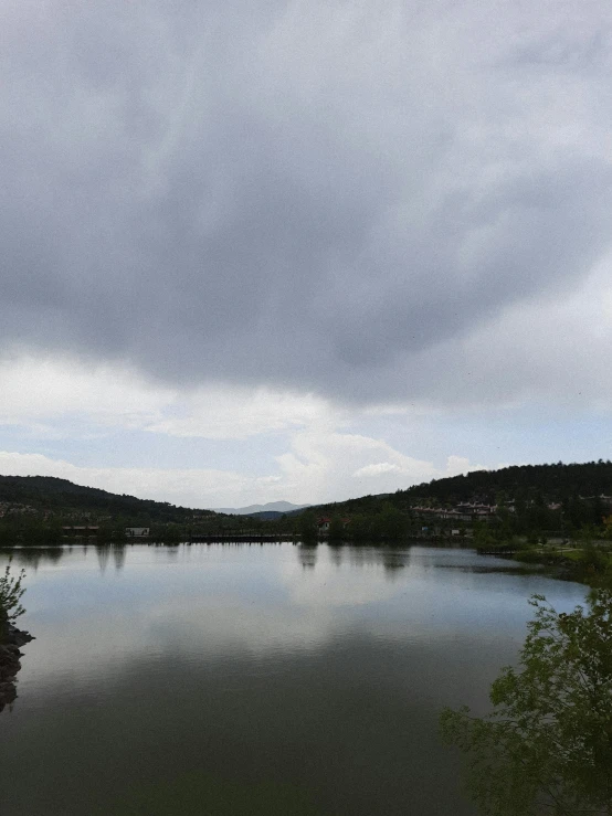 there is a lake surrounded by green trees and a dark sky