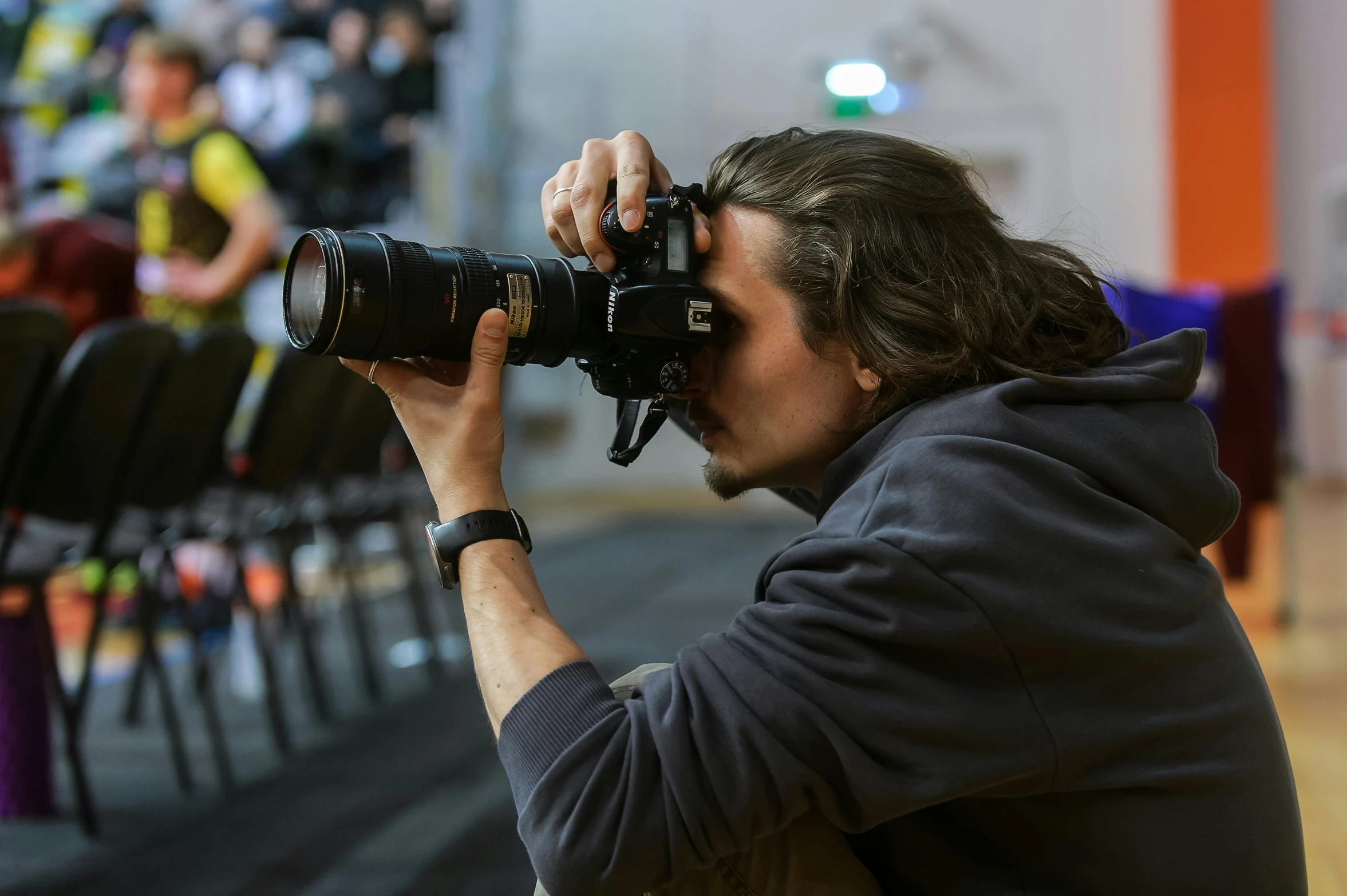 a man holding a large camera near some empty chairs