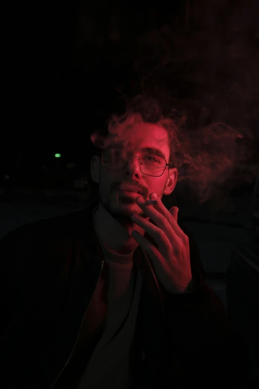 a man with glasses is smoking in the dark