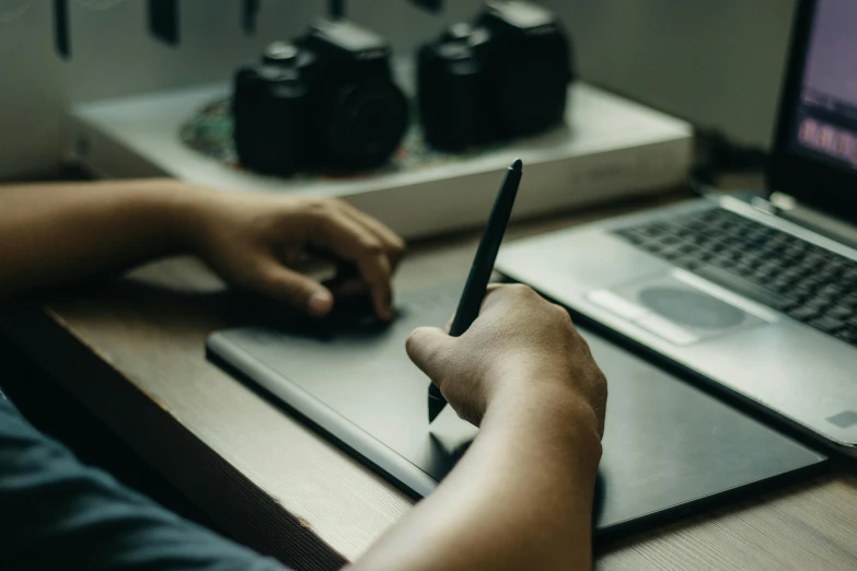 hand writing soing on the paper with the laptop beside him