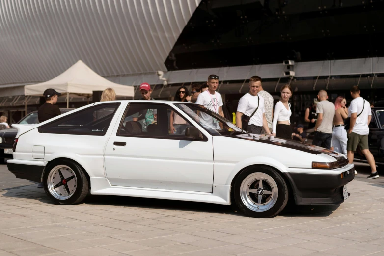 an old - school nissan is sitting on the pavement as people walk by it