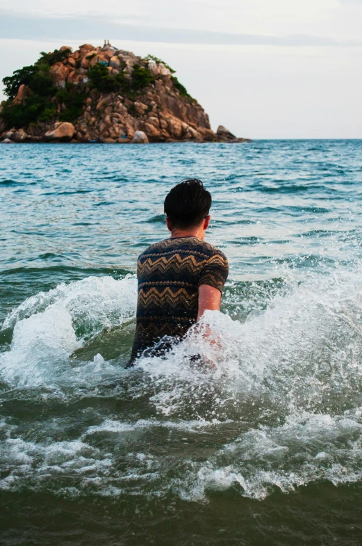 man is splashing up and to himself as he wades out into the water