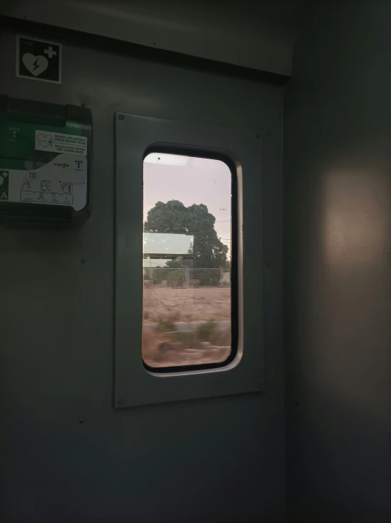 the window of a train car with trees and a field out the window