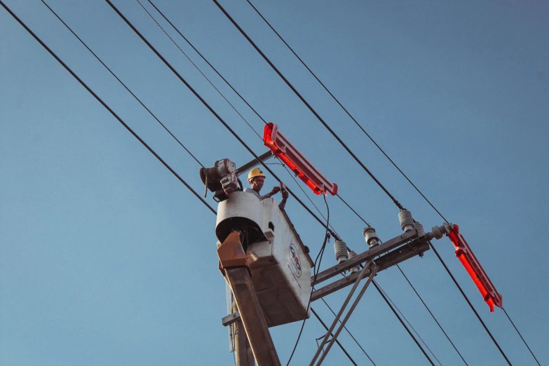 an electric worker on a high voltage pole is adjusting the lights on a telephone