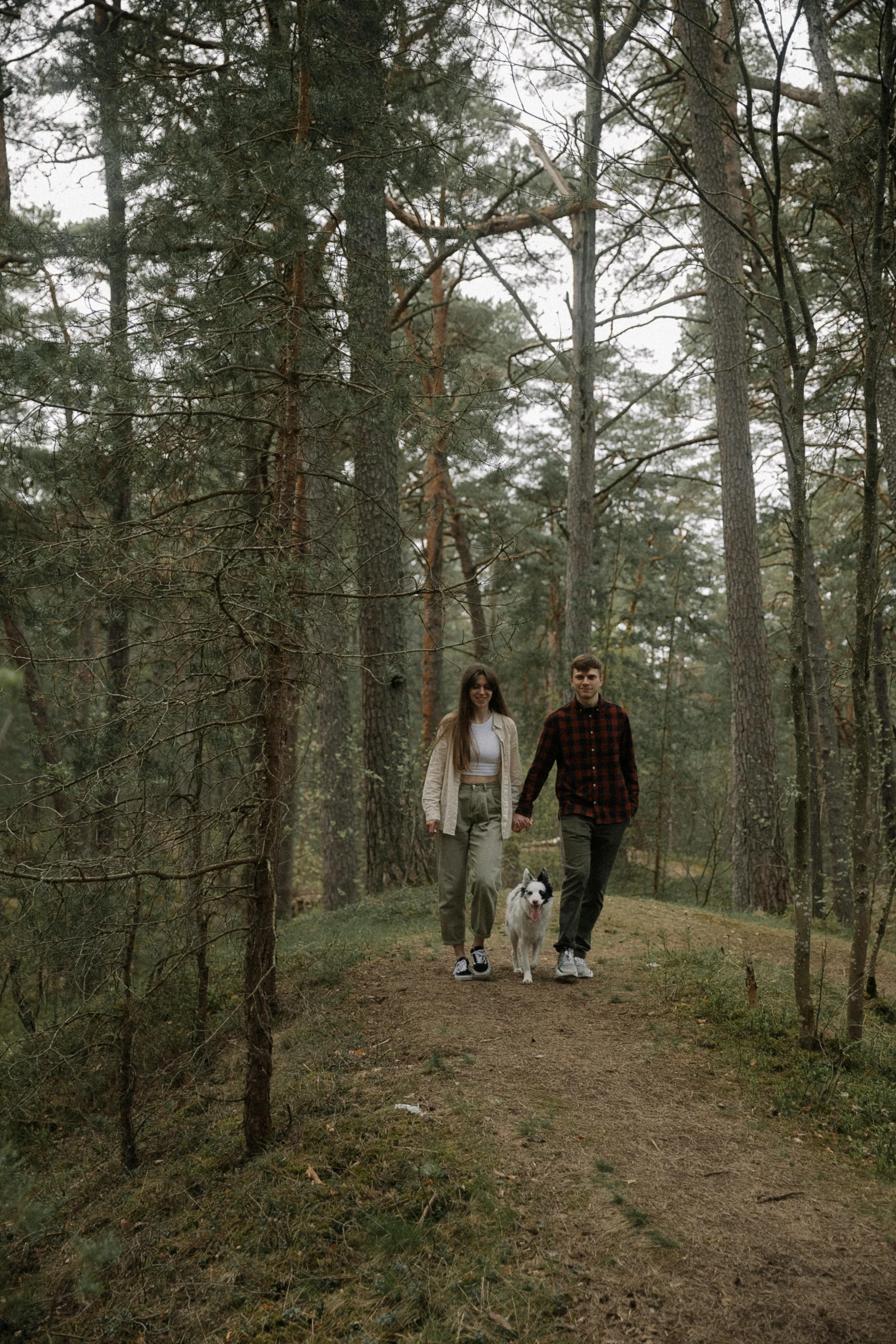 a couple walks down a dirt path holding hands while their dog watches