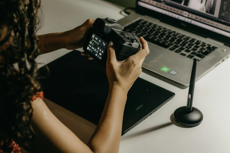 woman sitting at laptop, taking pictures with camera phone