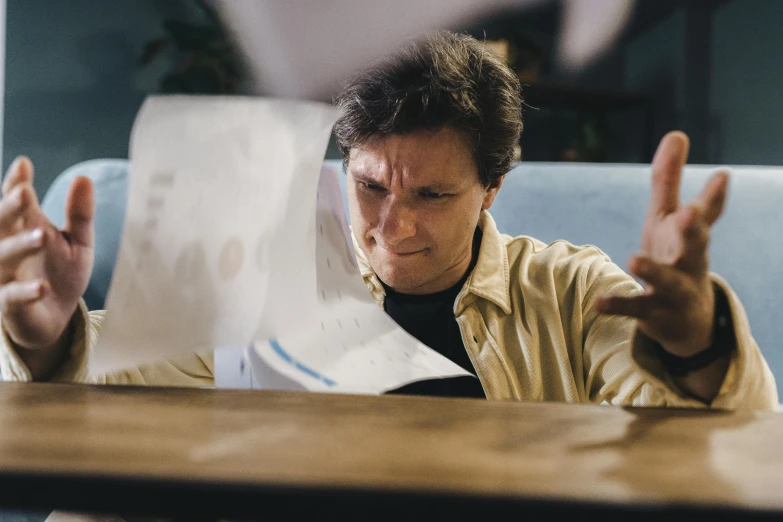 a man sitting at a table holding up papers and flipping a peace sign