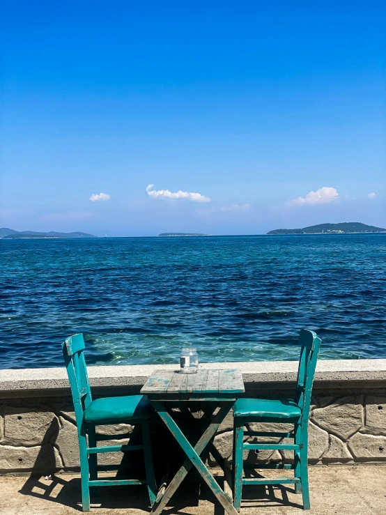 two green chairs and table are on the sand of a beach