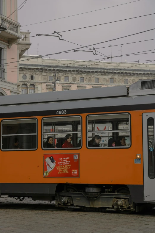 people are riding on the side of the street as the orange train sits idle