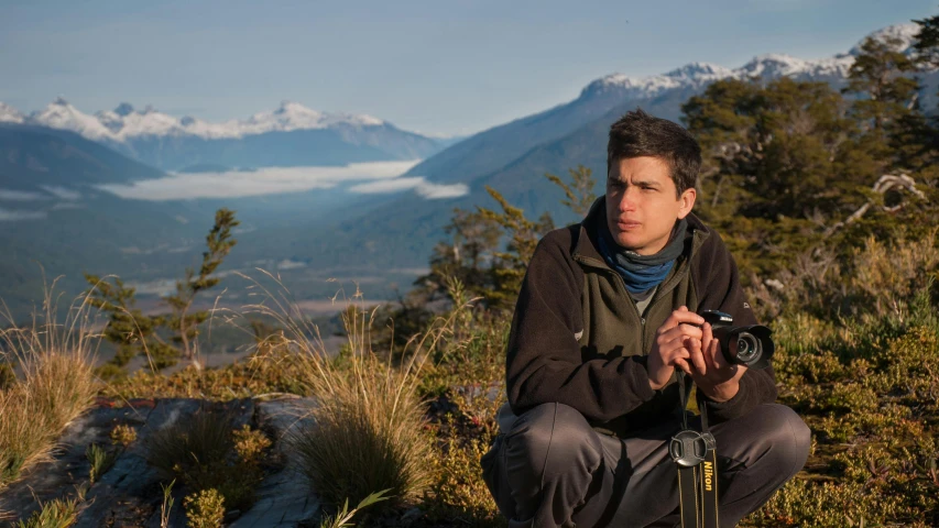 man with camera crouching on mountain in scenic environment