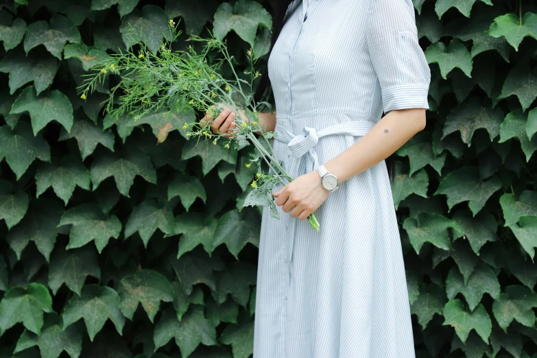 a woman holding some kind of flower standing in front of a plant wall