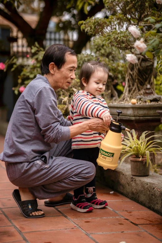 a man pouring water for a child in front of a potted plant