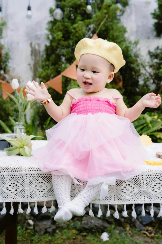 there is a baby girl that is dressed in a pink and yellow dress sitting on a table