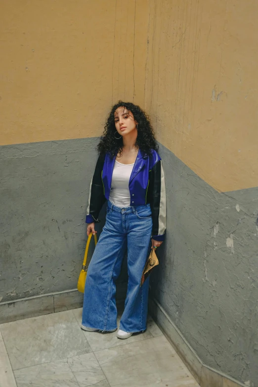 woman wearing blue jean overalls stands against a wall