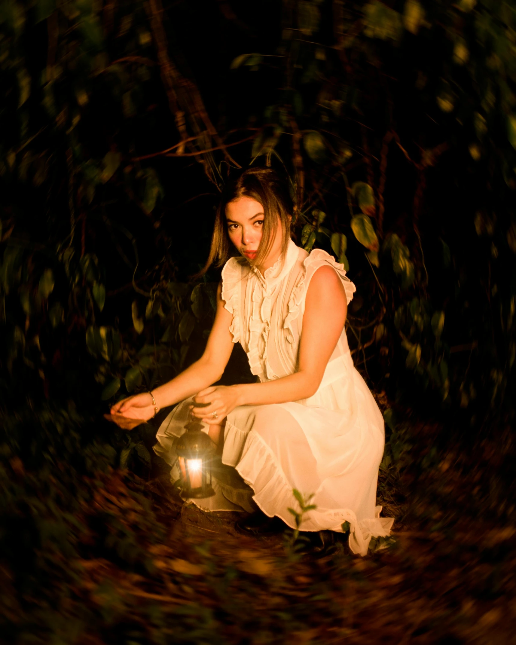 a woman with a lantern crouches down in the woods