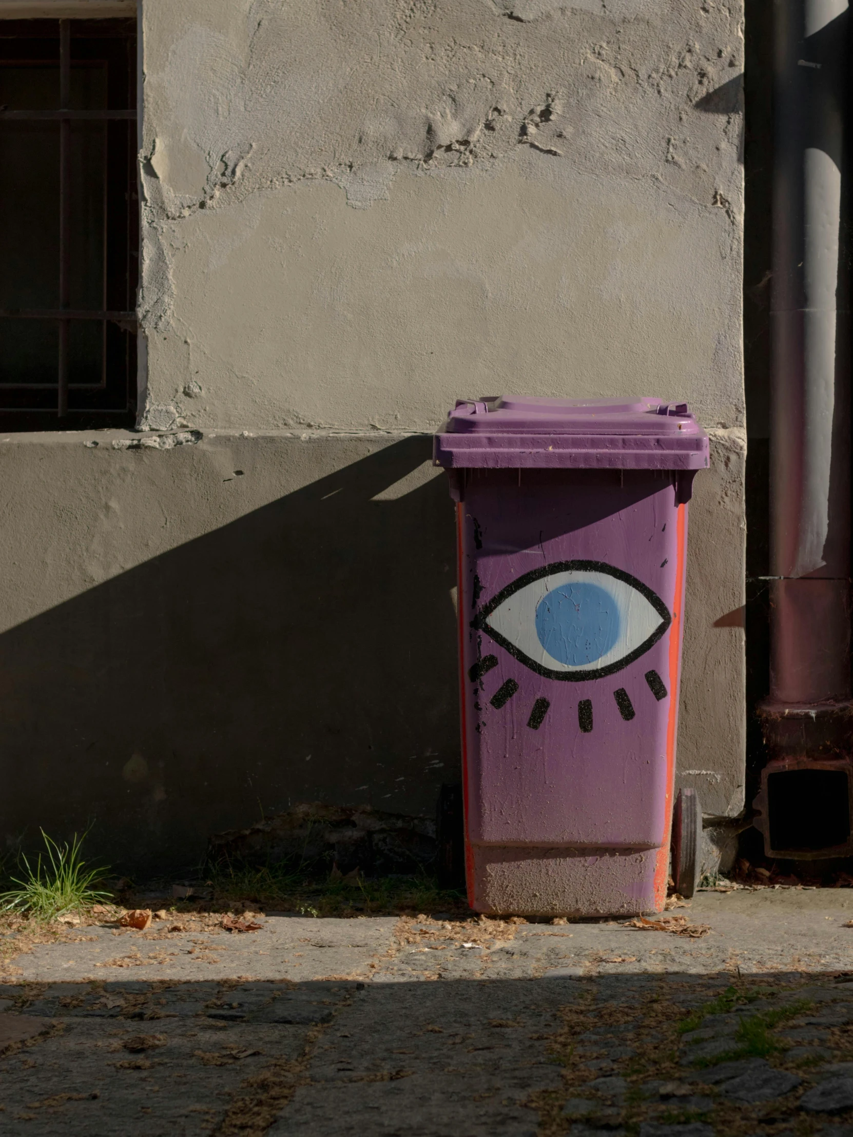 an odd purple bin with an eye painted on it next to a street light